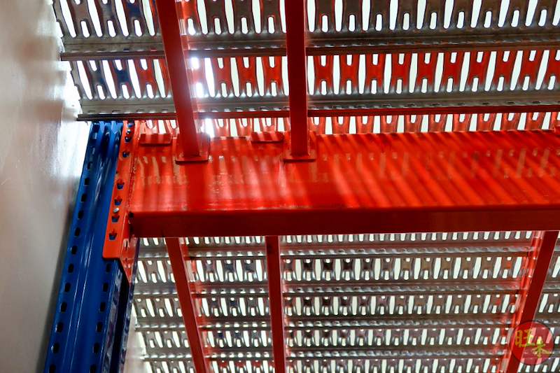 Red mezzanine beam bolted to a blue upright with perforated steel decking above, viewed from below - V6000 Racking - V6-7 | Wong Lye Racking, Singapore Racking Manufacturer