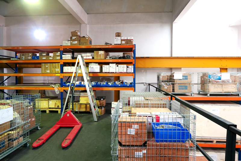 Mezzanine deck with racking bays of cartons, wire cages and a pallet truck, black edge railing beyond - V5000 Racking - V5-8 | Wong Lye Racking, Singapore Racking Manufacturer