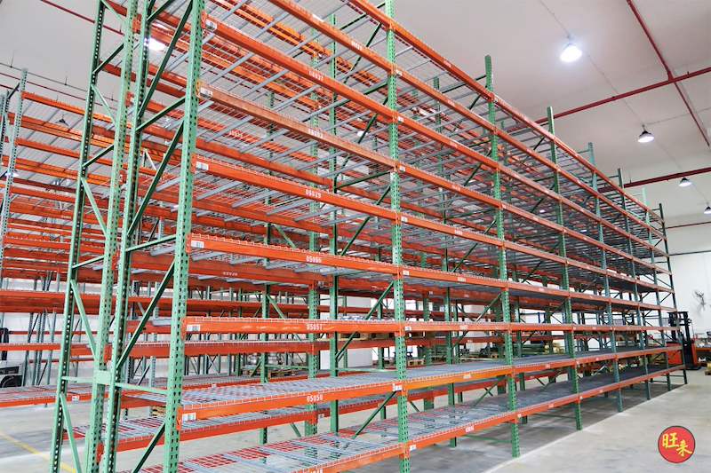 Tall pallet racking run with green uprights, orange beams and mesh decks under warehouse lighting - V3000 Racking - V3-3 | Wong Lye Racking, Singapore Racking Manufacturer