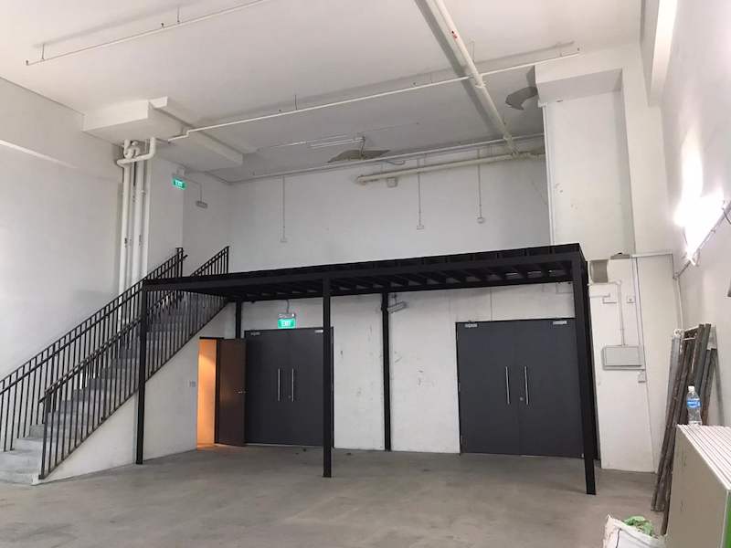 Black steel mezzanine platform on square columns over a doorway with a staircase and railing, unit otherwise empty - V5000 Racking - V5-9 | Wong Lye Racking, Singapore Racking Manufacturer