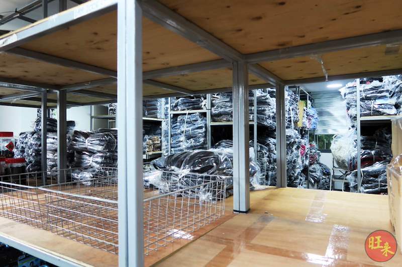 Underside of a mezzanine floor showing steel columns and beams supporting a plywood deck, with wire mesh baskets and bagged garments stored beneath - V8000 Racking - V8-20 | Wong Lye Racking, Singapore Racking Manufacturer