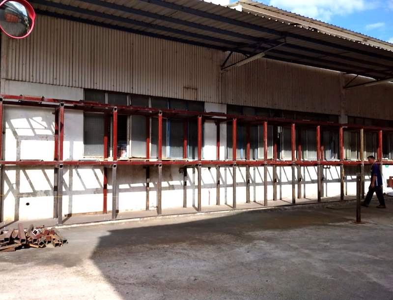 Welded steel rack frame with uprights and beams erected along an outdoor wall under a shed roof, bays still empty - V5000 Racking - V5-1 | Wong Lye Racking, Singapore Racking Manufacturer