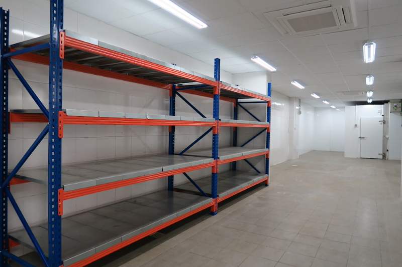 Run of long-span racking with orange beams and steel deck panels against the wall of a tiled room - Boltless Racking - B5 | Wong Lye Racking, Singapore Racking Manufacturer
