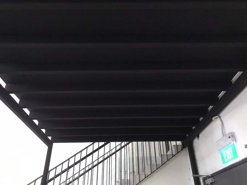 Black steel mezzanine beams and joists from below, with the staircase railing beside an exit sign - V5000 Racking - V5-9 | Wong Lye Racking, Singapore Racking Manufacturer
