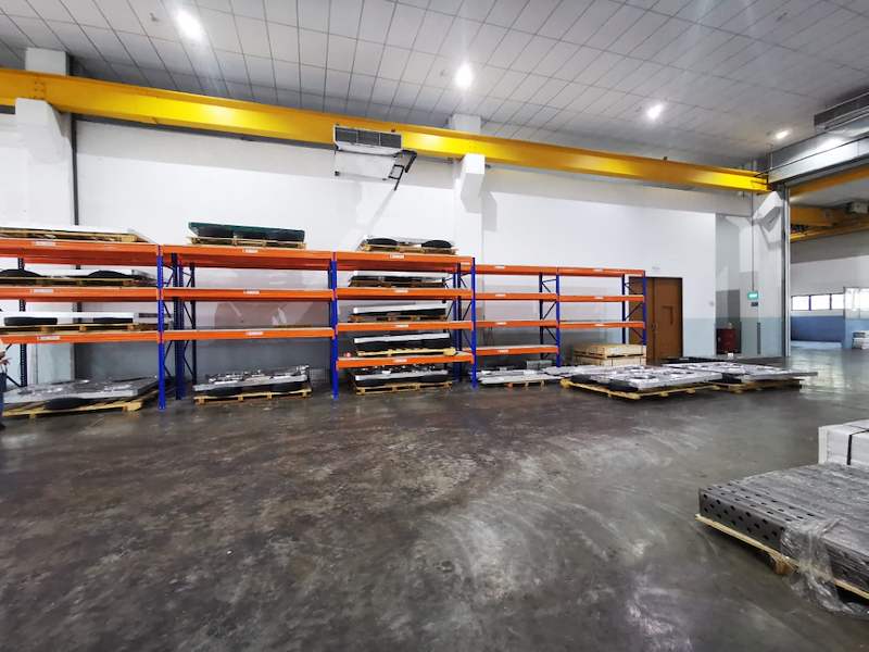 Run of V3000 racking bays along a workshop wall with steel parts on the decks and on pallets below - V3000 Racking - V3-1 | Wong Lye Racking, Singapore Racking Manufacturer