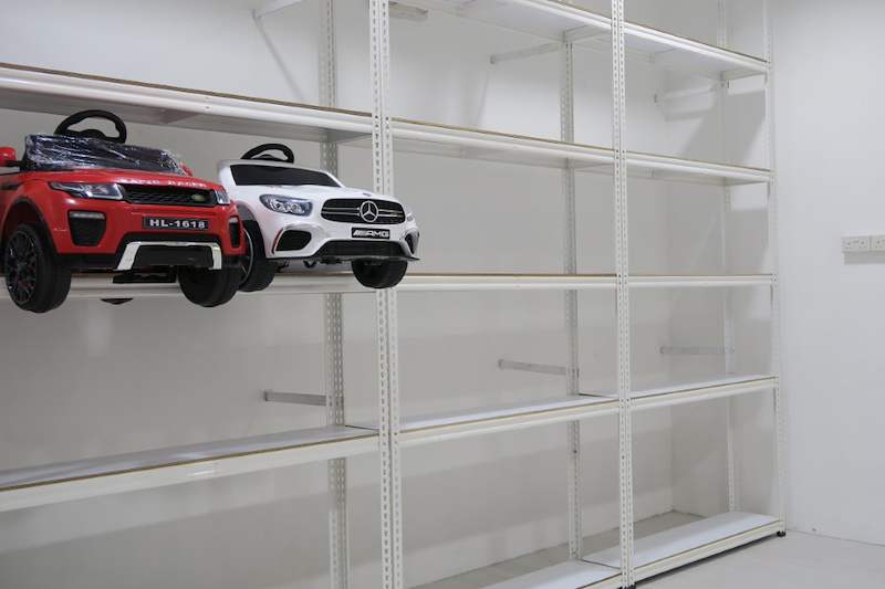 Two ride-on toy cars on a white boltless shelving level, shelves above and below empty - Boltless Racking - B3 | Wong Lye Racking, Singapore Racking Manufacturer