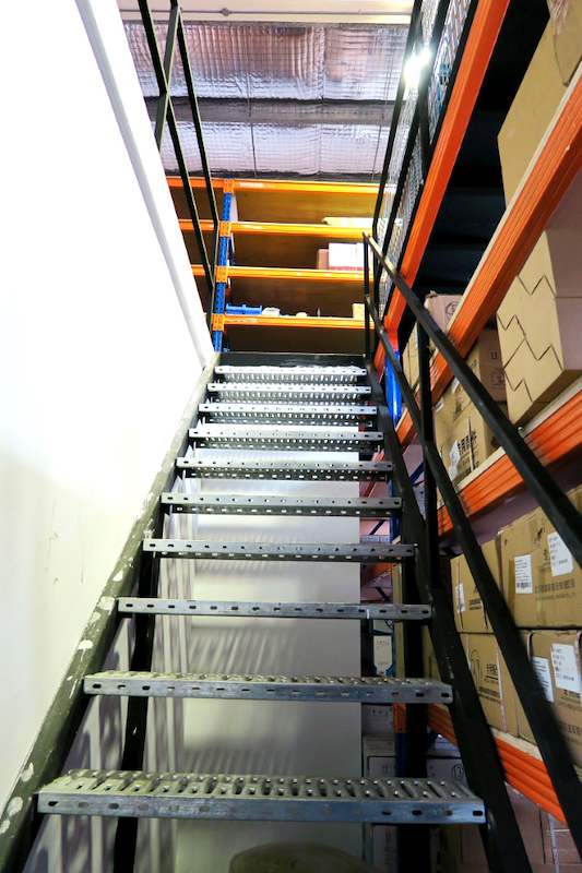 Staircase with perforated steel treads and black handrail rising to the racking on the mezzanine - V5000 Racking - V5-8 | Wong Lye Racking, Singapore Racking Manufacturer