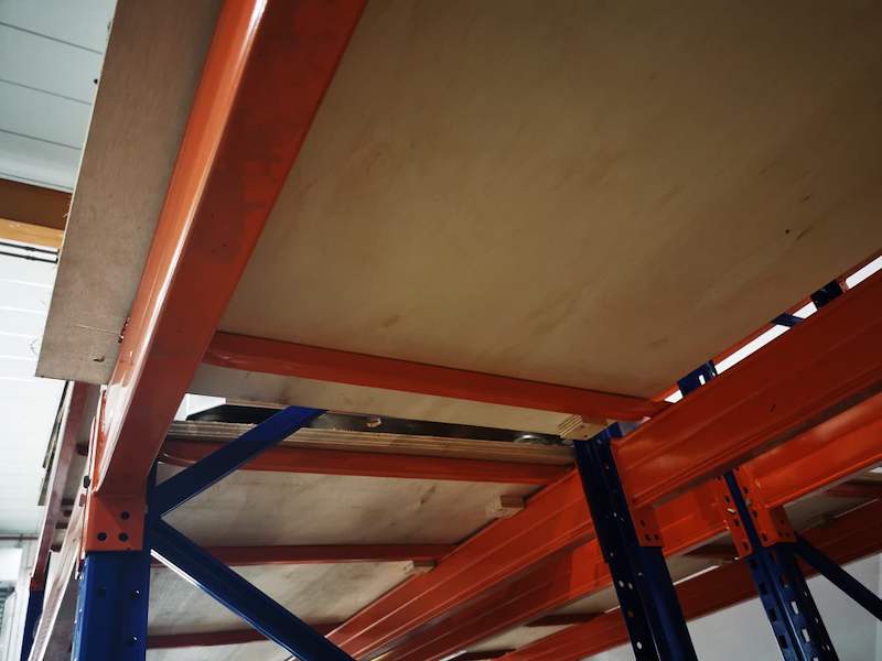 Plywood deck panel resting on orange beams and cross supports between blue uprights, viewed from below - V3000 Racking - V3-1 | Wong Lye Racking, Singapore Racking Manufacturer
