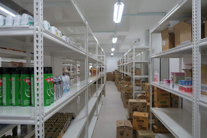 Aisle between white boltless shelving units with drinks and cartons, more stock on the floor - Boltless Racking - B6 | Wong Lye Racking, Singapore Racking Manufacturer