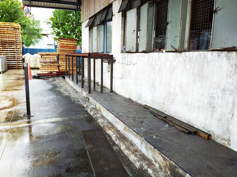Row of steel uprights on a base plate along the wall, seen from the yard, with timber pallets stacked beyond - V5000 Racking - V5-1 | Wong Lye Racking, Singapore Racking Manufacturer