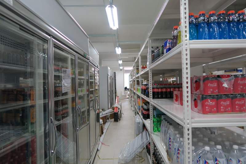 Aisle between glass-door chillers and white boltless shelving stocked with bottled drinks - Boltless Racking - B6 | Wong Lye Racking, Singapore Racking Manufacturer