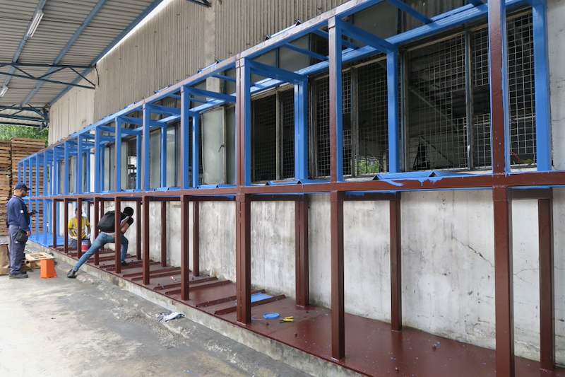 Steel rack frame in blue and red-oxide primer under construction along the wall, installers working at the base - V5000 Racking - V5-1 | Wong Lye Racking, Singapore Racking Manufacturer