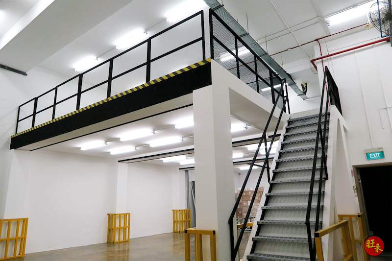Mezzanine floor structure seen from ground level: black railing and mesh fence on the deck, staircase to one side and yellow floor barriers - V8000 Racking - V8-6 | Wong Lye Racking, Singapore Racking Manufacturer