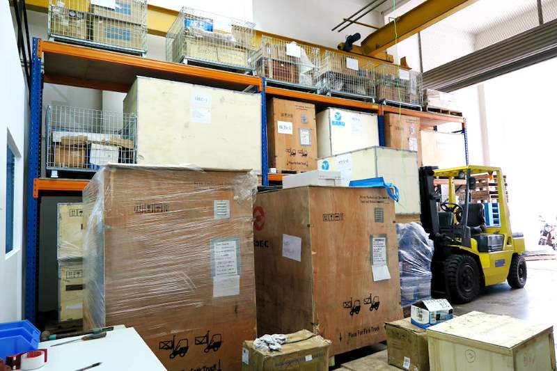 Blue-and-orange racking bays holding wire cages and cartons beside timber crates and a forklift - V5000 Racking - V5-8 | Wong Lye Racking, Singapore Racking Manufacturer