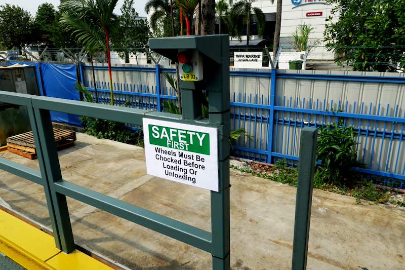 Steel railing with a safety sign at the edge of the loading platform, boundary fence behind - V10000 Racking - V10-1 | Wong Lye Racking, Singapore Racking Manufacturer