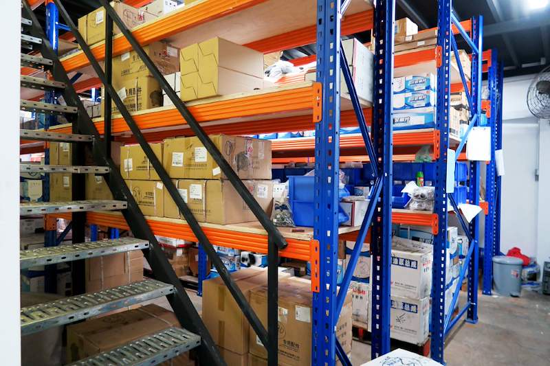 Steel staircase to the mezzanine beside blue-and-orange racking loaded with cartons - V5000 Racking - V5-8 | Wong Lye Racking, Singapore Racking Manufacturer